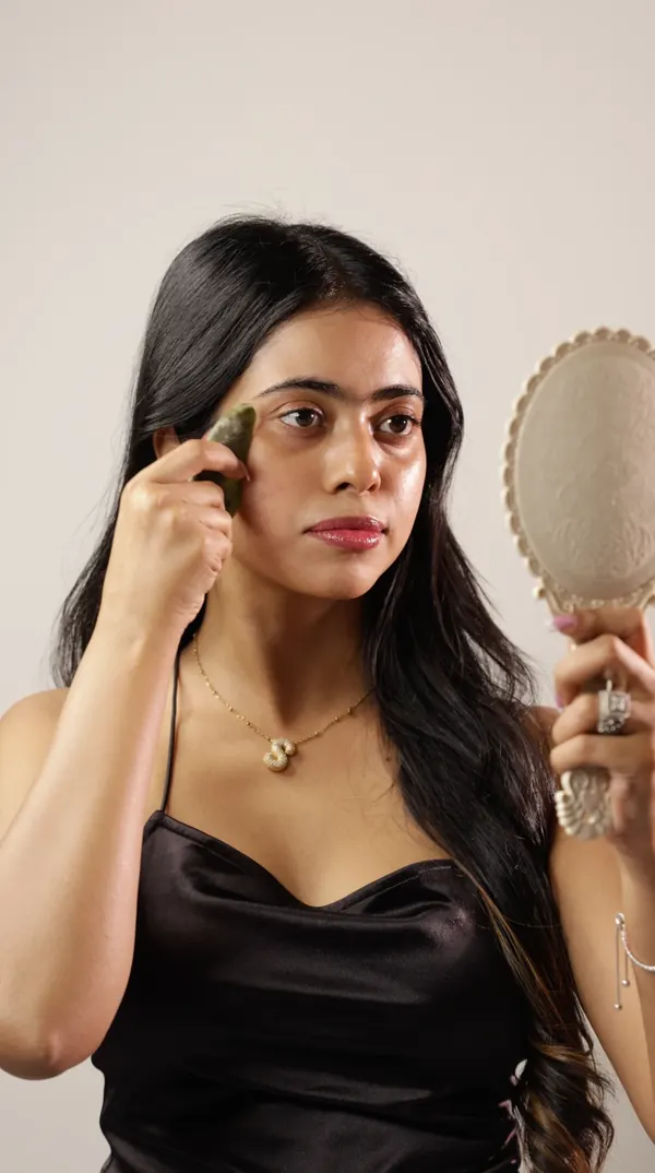 Sandipta using a gua sha while holding a hand mirror